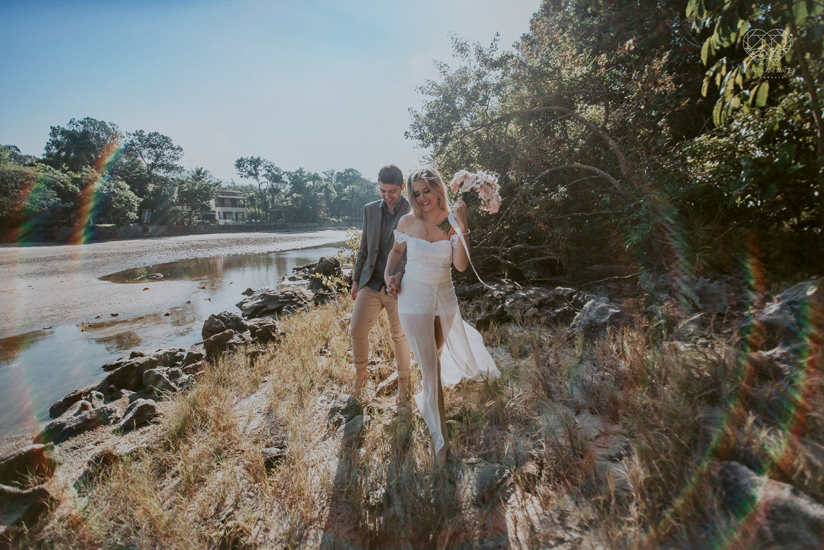ensaio pre casamento pre wedding na praia das conchas no guaruja noiva de roupa branca e buque e noivo com roupa sociall fotos feitas na agua  na grama e correndo nas pedras ensaio feito pela fotografa premiada nayara andrade de santos