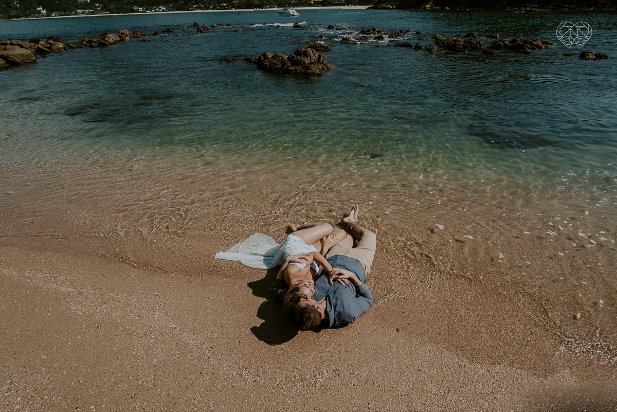 ensaio pre casamento pre wedding na praia das conchas no guaruja noiva de roupa branca e buque e noivo com roupa sociall fotos feitas na agua  na grama e correndo nas pedras ensaio feito pela fotografa premiada nayara andrade de santos