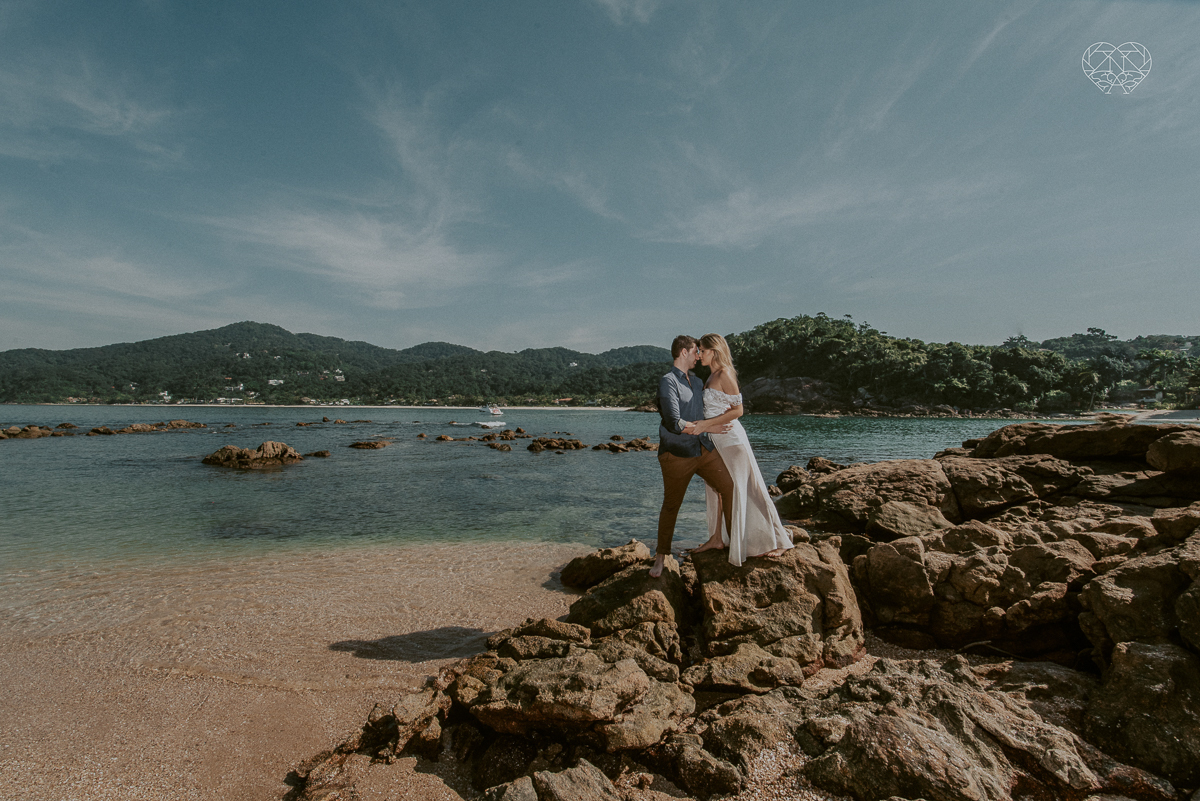 ensaio pre casamento pre wedding na praia das conchas no guaruja noiva de roupa branca e buque e noivo com roupa sociall fotos feitas na agua  na grama e correndo nas pedras ensaio feito pela fotografa premiada nayara andrade de santos