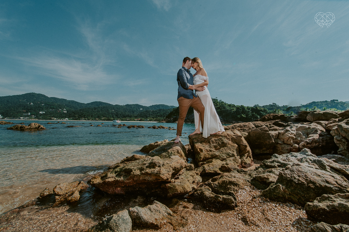 ensaio pre casamento pre wedding na praia das conchas no guaruja noiva de roupa branca e buque e noivo com roupa sociall fotos feitas na agua  na grama e correndo nas pedras ensaio feito pela fotografa premiada nayara andrade de santos