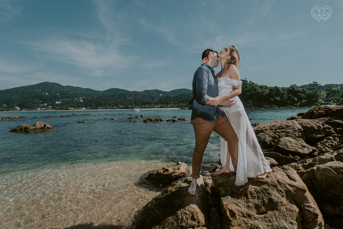 ensaio pre casamento pre wedding na praia das conchas no guaruja noiva de roupa branca e buque e noivo com roupa sociall fotos feitas na agua  na grama e correndo nas pedras ensaio feito pela fotografa premiada nayara andrade de santos