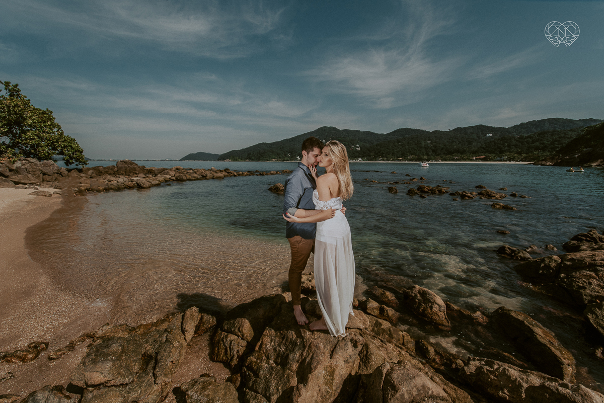 ensaio pre casamento pre wedding na praia das conchas no guaruja noiva de roupa branca e buque e noivo com roupa sociall fotos feitas na agua  na grama e correndo nas pedras ensaio feito pela fotografa premiada nayara andrade de santos