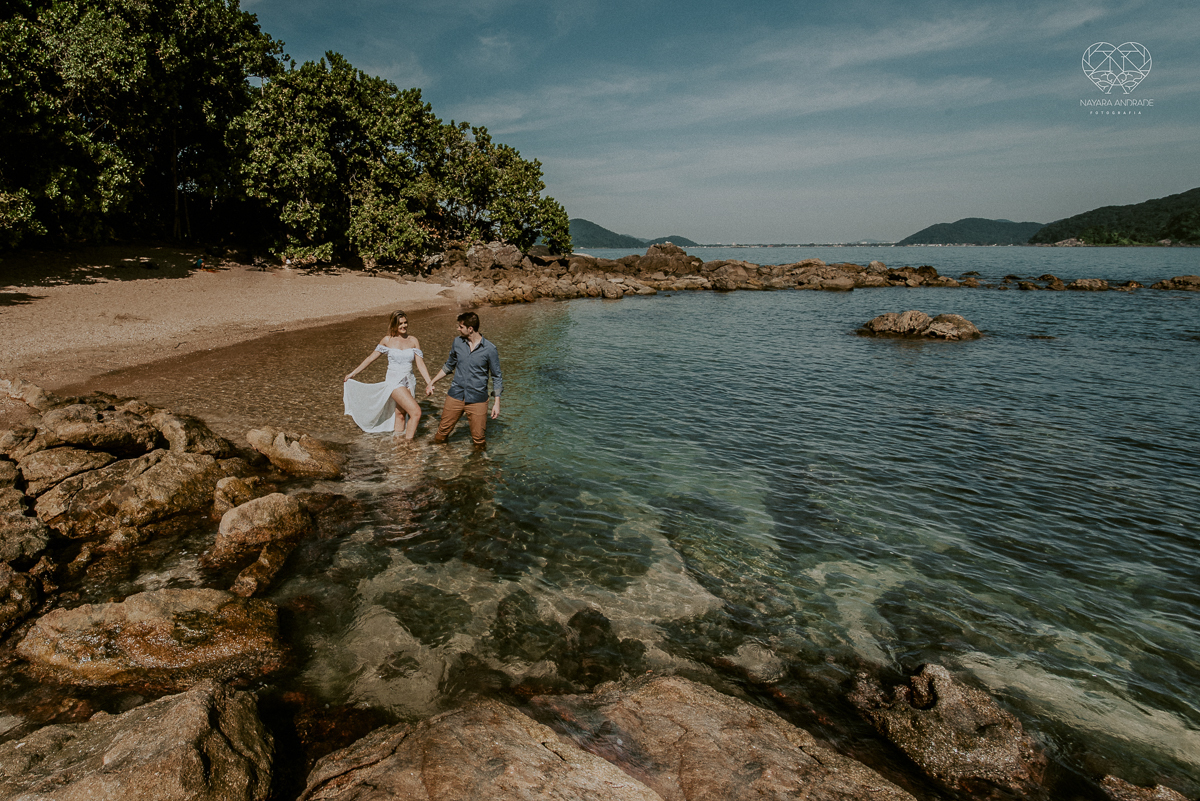 ensaio pre casamento pre wedding na praia das conchas no guaruja noiva de roupa branca e buque e noivo com roupa sociall fotos feitas na agua  na grama e correndo nas pedras ensaio feito pela fotografa premiada nayara andrade de santos