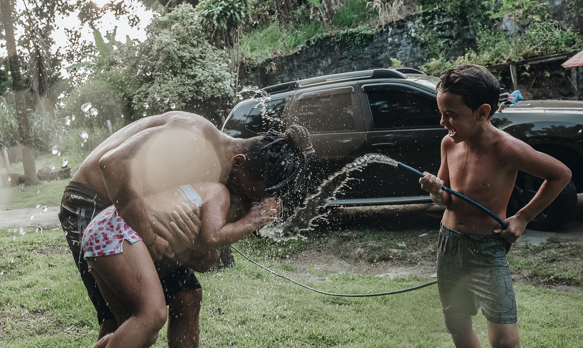 ensaio familia lifestyle brincando de mangueira no quintal de casa com o papai crianças e o cachorro fotografado pela fotografa premiada nayara andrade nayara andrade fotografia