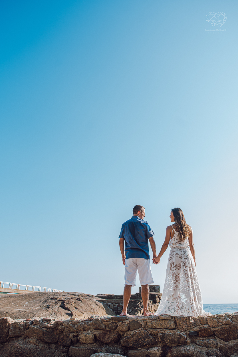 fotografia pre wedding de casal na praia noiva de vestido branco casal fazendo fotos em poses inspiração pela fotografa nayara andrade lindo por do sol colorido e fotos artisticas pela fotografa premiada mundialmente casamentos de dia inspiração