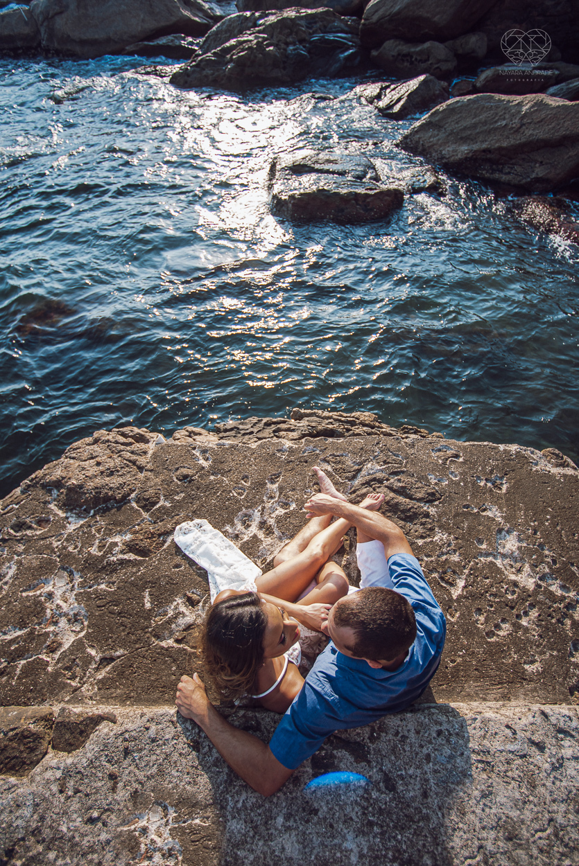 fotografia pre wedding de casal na praia noiva de vestido branco casal fazendo fotos em poses inspiração pela fotografa nayara andrade lindo por do sol colorido e fotos artisticas pela fotografa premiada mundialmente casamentos de dia inspiração