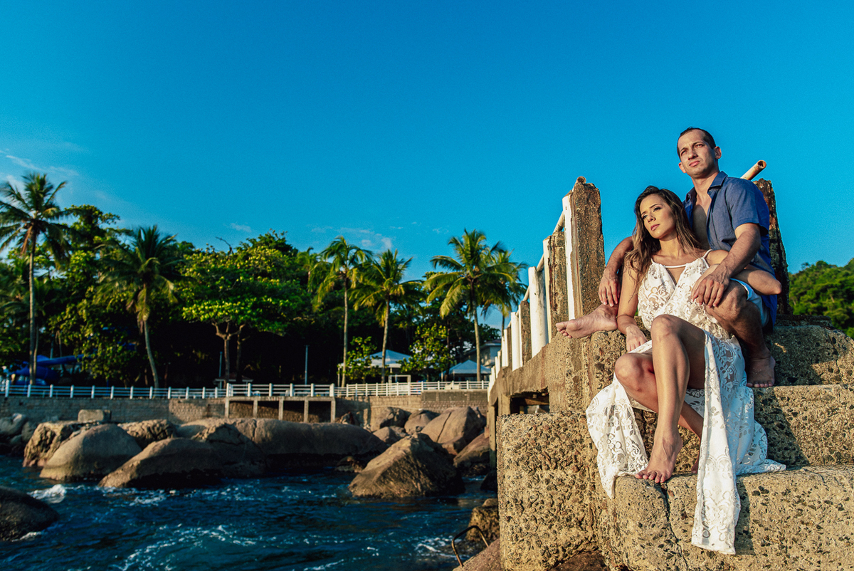fotografia pre wedding de casal na praia noiva de vestido branco casal fazendo fotos em poses inspiração pela fotografa nayara andrade lindo por do sol colorido e fotos artisticas pela fotografa premiada mundialmente casamentos de dia inspiração