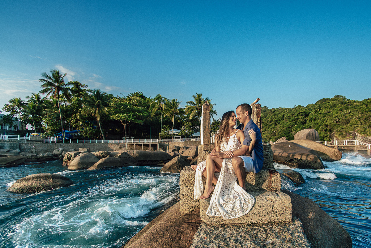 fotografia pre wedding de casal na praia noiva de vestido branco casal fazendo fotos em poses inspiração pela fotografa nayara andrade lindo por do sol colorido e fotos artisticas pela fotografa premiada mundialmente casamentos de dia inspiração