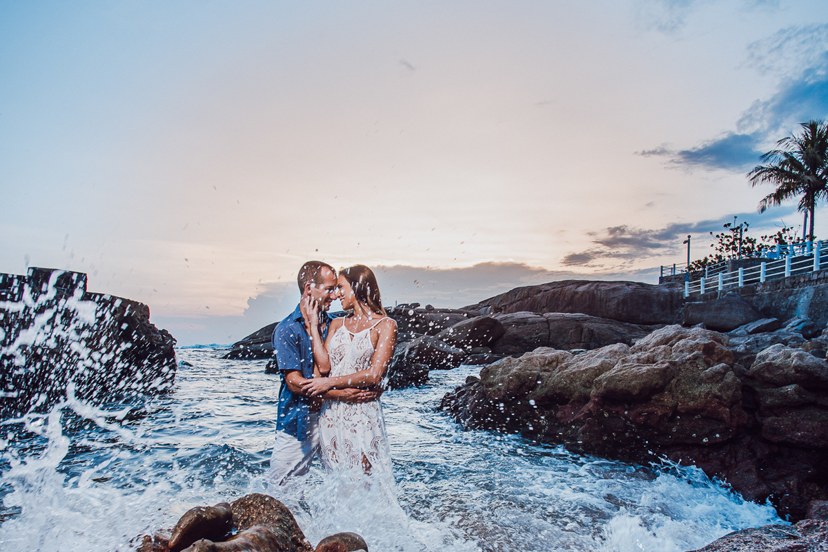 fotografia pre wedding de casal na praia noiva de vestido branco casal fazendo fotos em poses inspiração pela fotografa nayara andrade lindo por do sol colorido e fotos artisticas pela fotografa premiada mundialmente casamentos de dia inspiração