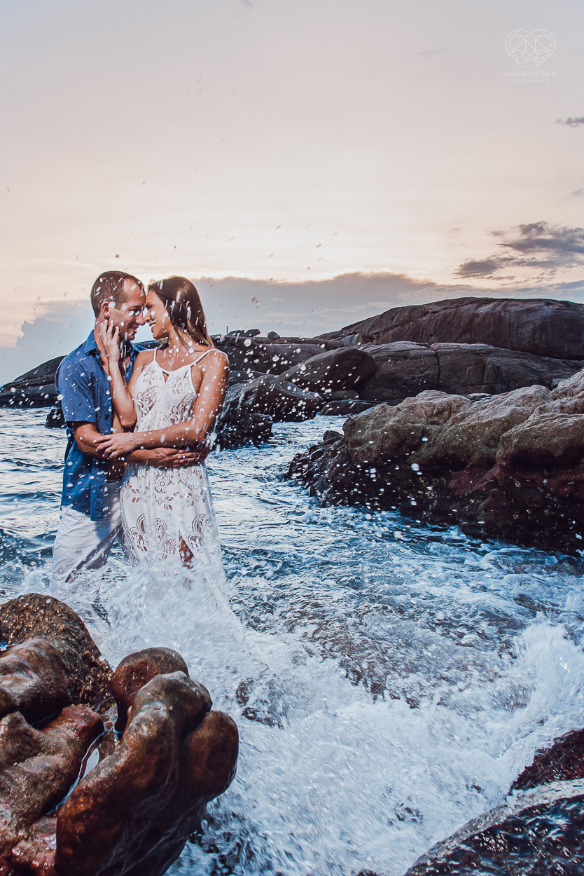 fotografia pre wedding de casal na praia noiva de vestido branco casal fazendo fotos em poses inspiração pela fotografa nayara andrade lindo por do sol colorido e fotos artisticas pela fotografa premiada mundialmente casamentos de dia inspiração