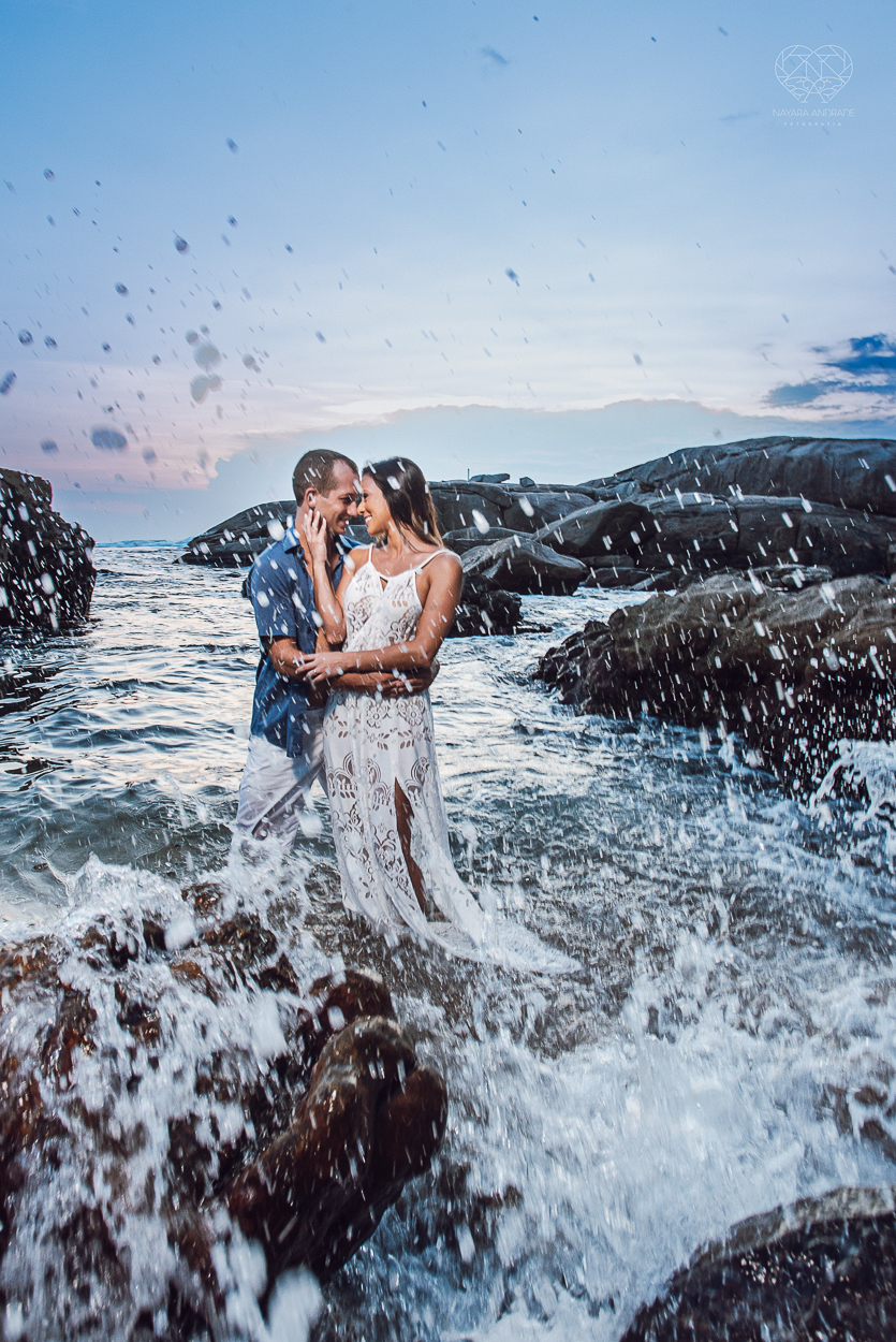 fotografia pre wedding de casal na praia noiva de vestido branco casal fazendo fotos em poses inspiração pela fotografa nayara andrade lindo por do sol colorido e fotos artisticas pela fotografa premiada mundialmente casamentos de dia inspiração