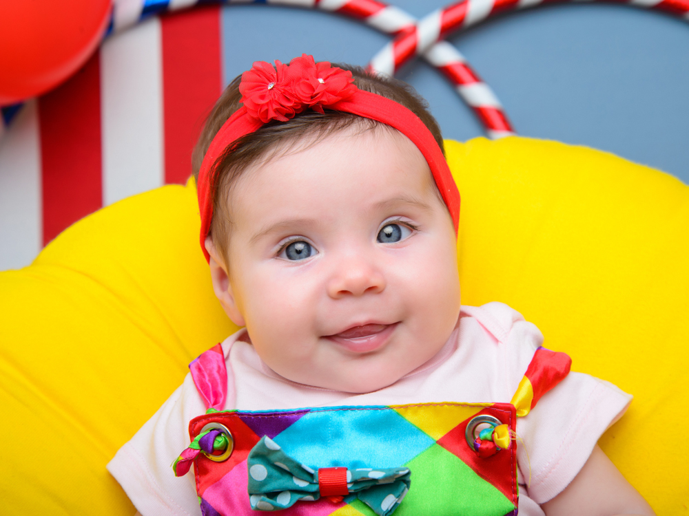 sessão circo, macacão colorido, olhos azuis, laço vermelho, flores.