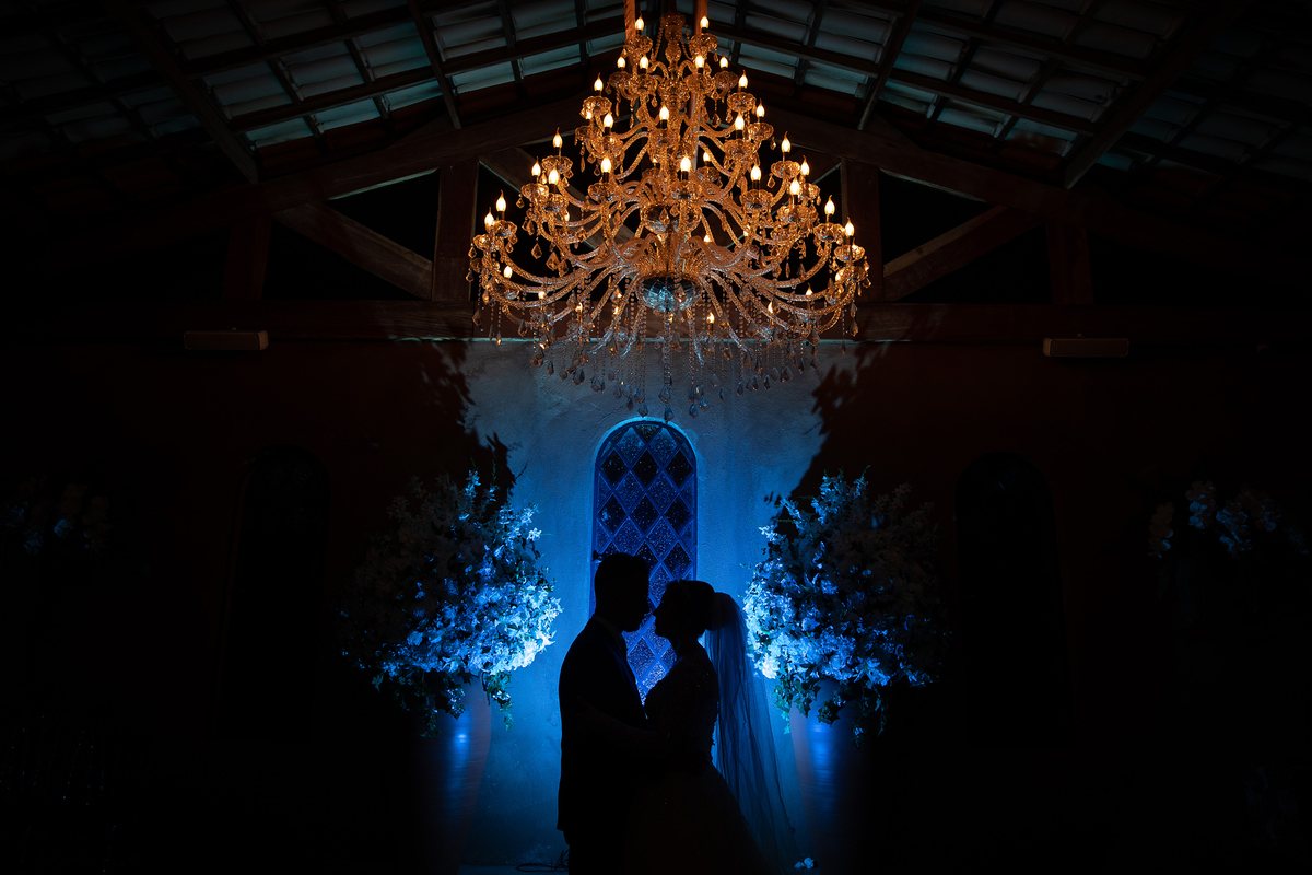 Ensaio pós cerimônia, uma bela silhueta com um fundo azul e a iluminação do lustre bem quente para dar um belo contraste de cores