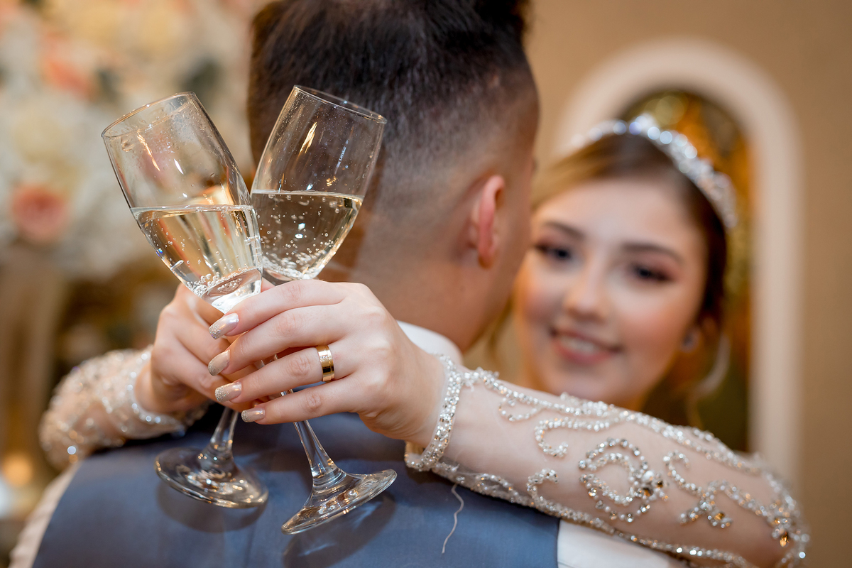 Noiva abraçando o noivo com as taças do espumante em suas costas 