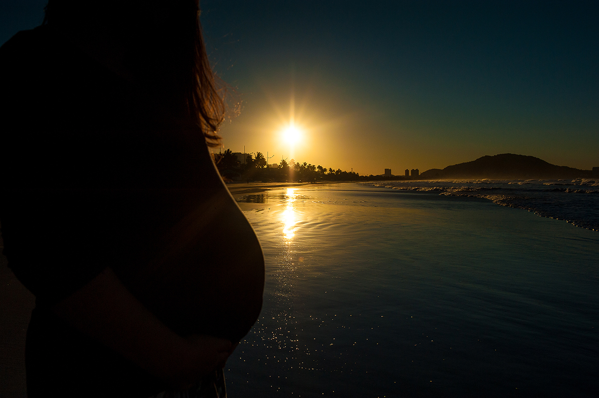 foto do nascer do som com a gestante mostrando a barriga, sessão de fotos de grávida.