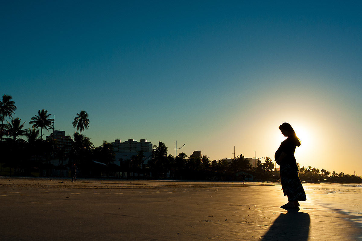 Nascer do sol na praia de Guarujá, com uma silhueta de gestante.