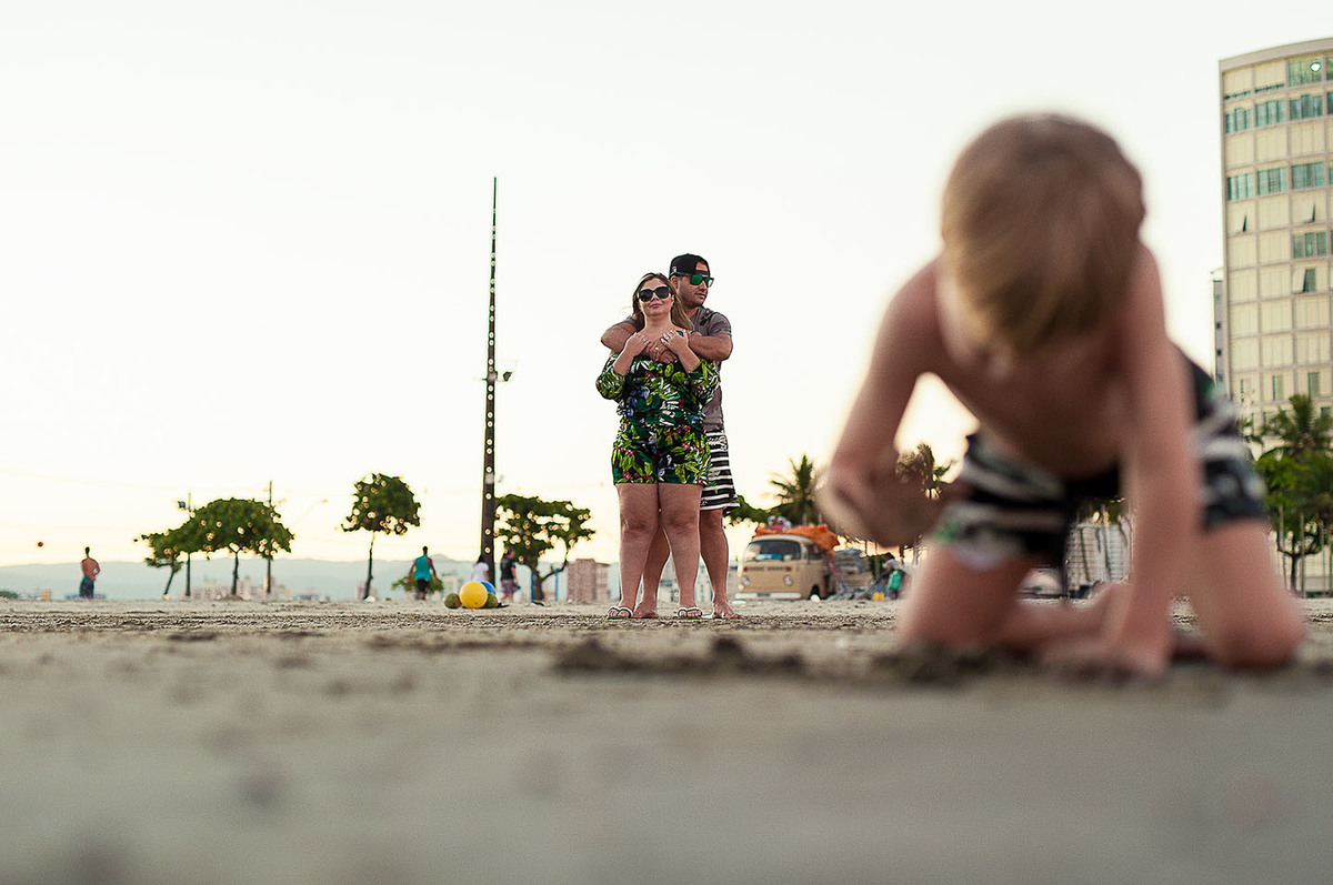 foto Ilha do Porchat - santos - praia de são vicente - fotografia Paulo Araujo, ensaio de família, lifestyle, criança fazendo castelo de areia e os pais olhando.