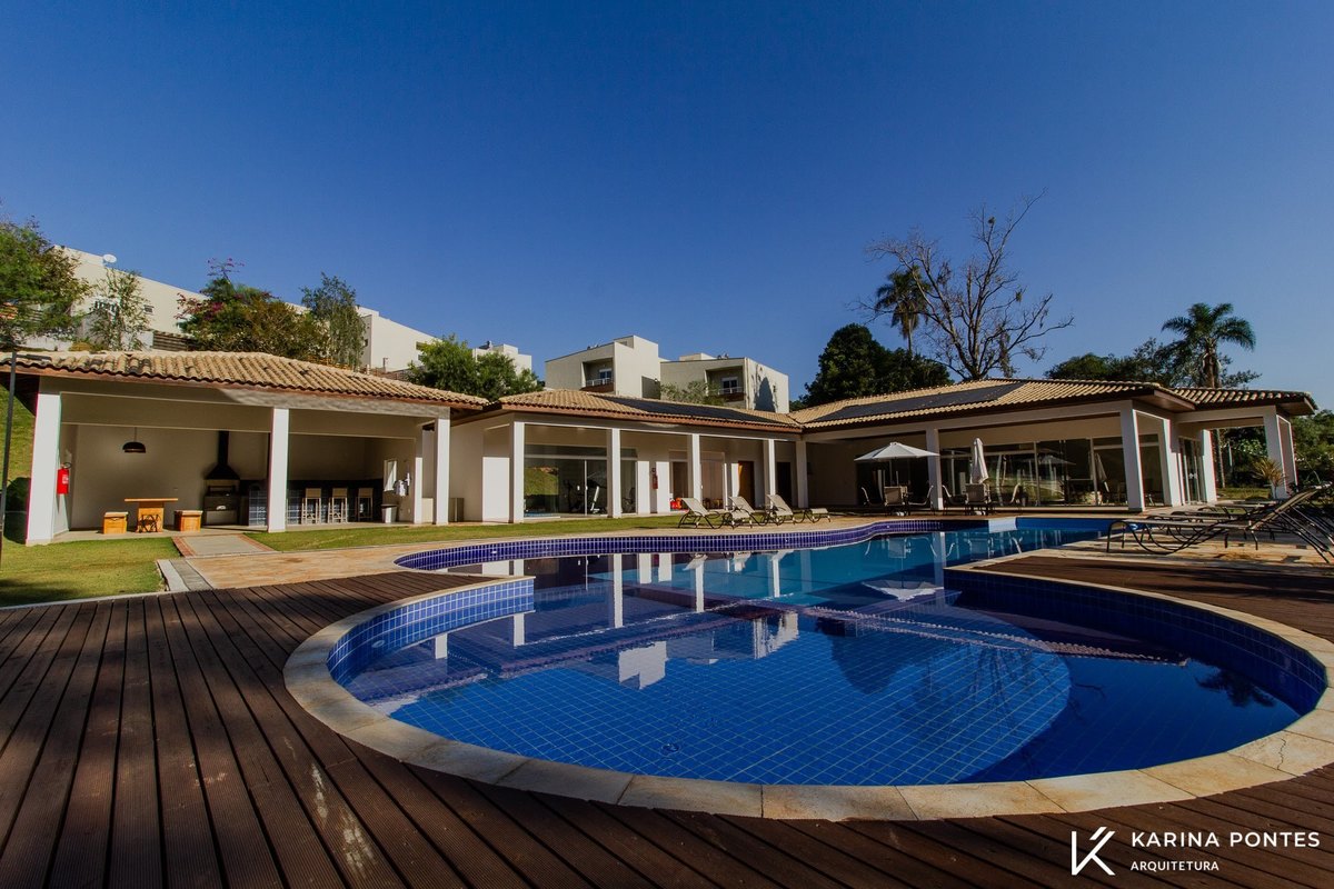 #ParaCegoVer: Fotografia da piscina, ao fundo área gourmet e residência do Condomínio Ecovillagio