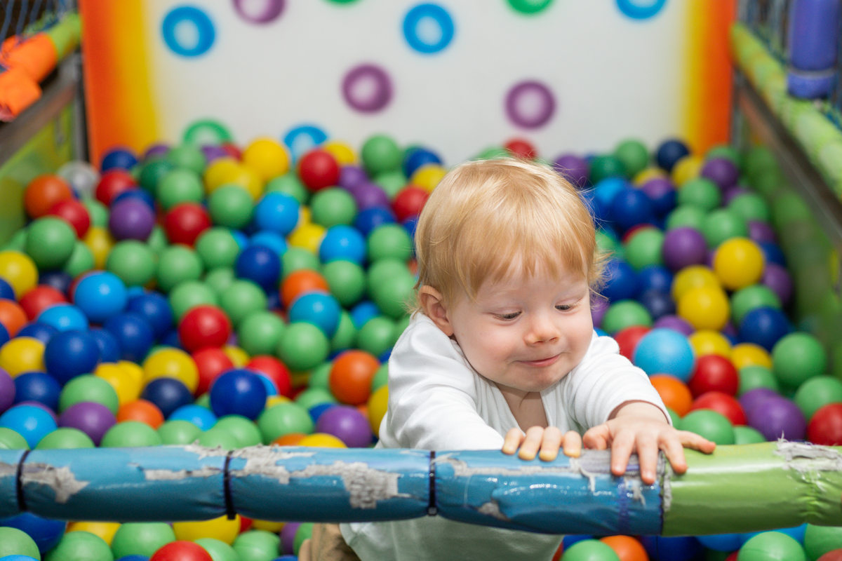 Foto do aniversariante agarrado à um brinquedo com cara de arteiro, bolinhas coloridas ao fundo.