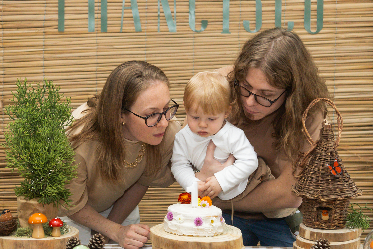 Foto da mamãe, aniversariante e Papai soprando a velinha do bolo.