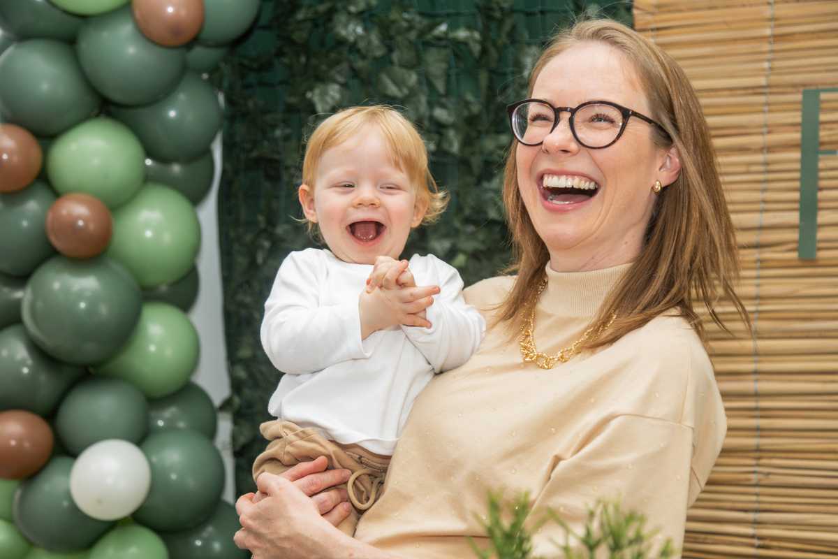 Foto do aniversáriante no colo da mãe, ambos dando uma grande gargalhada.