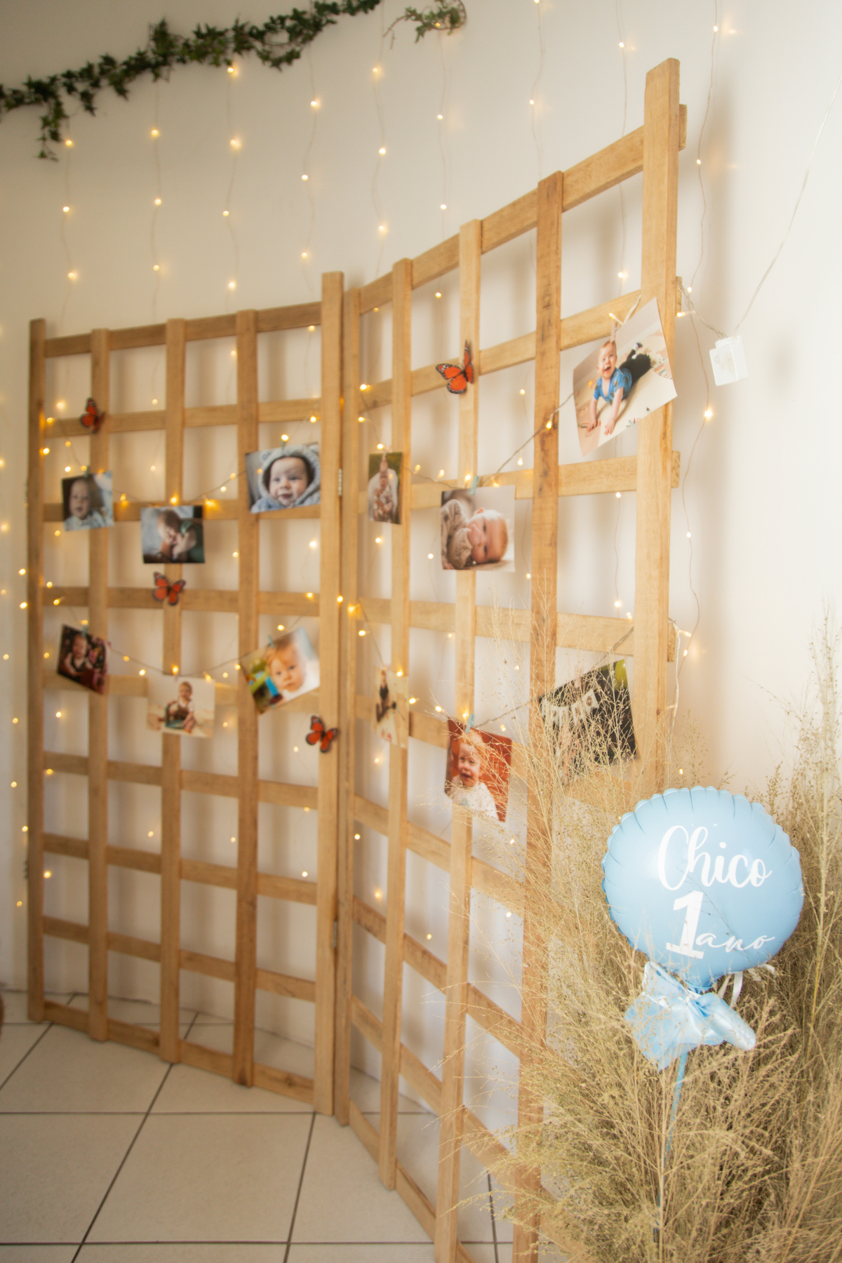 Foto do painel de madeira na entrada da festa com muitas luzinhas e um varal de fotos do aniversariante.