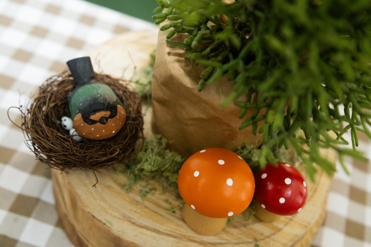 Foto de detalhe da decoração mostrando um vaso com uma suculenta, cogumelos coloridos e um ninho de passarinho.