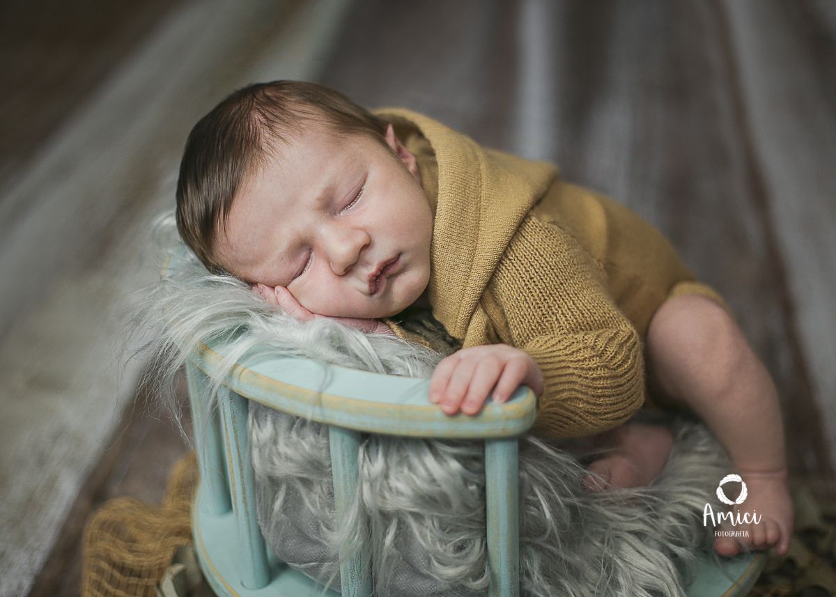 Fotografia de recém nascido, bebê deitado de lado em prop estilo banquinho na cor azul bebê.
