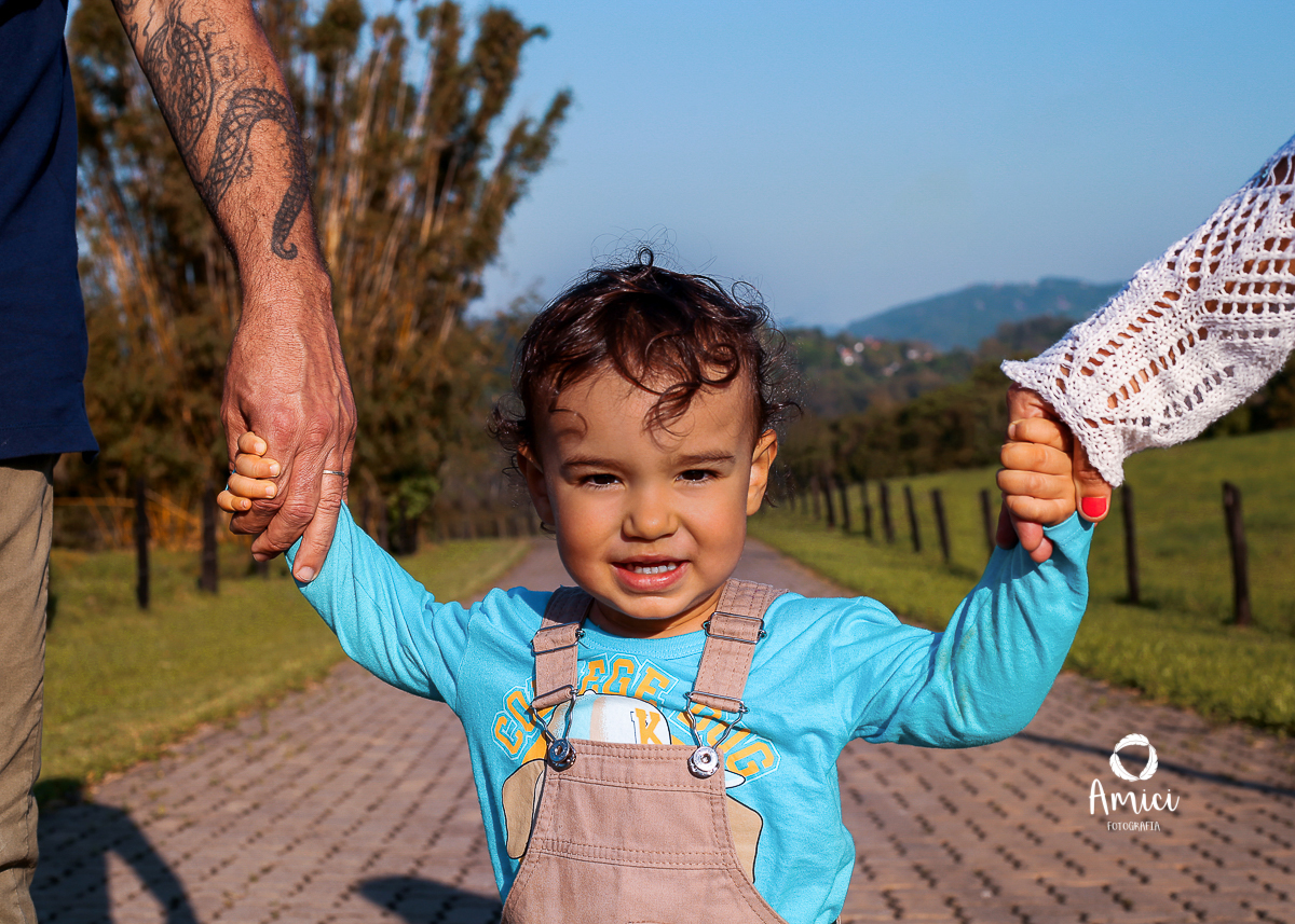 Fotografia Infantil, destaque no rosto do menino, de mãos dadas com os pais.