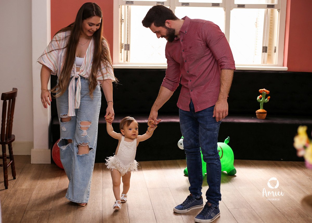 Foto de família, bebê caminhando de mãos dadas com os pais.