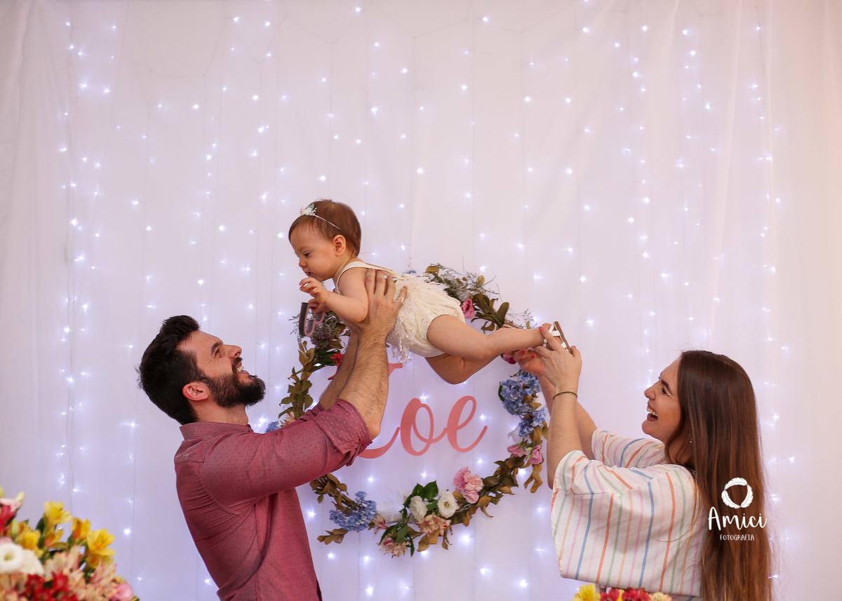Fotografia infantil, pai e mãe elevando bebê para cima.