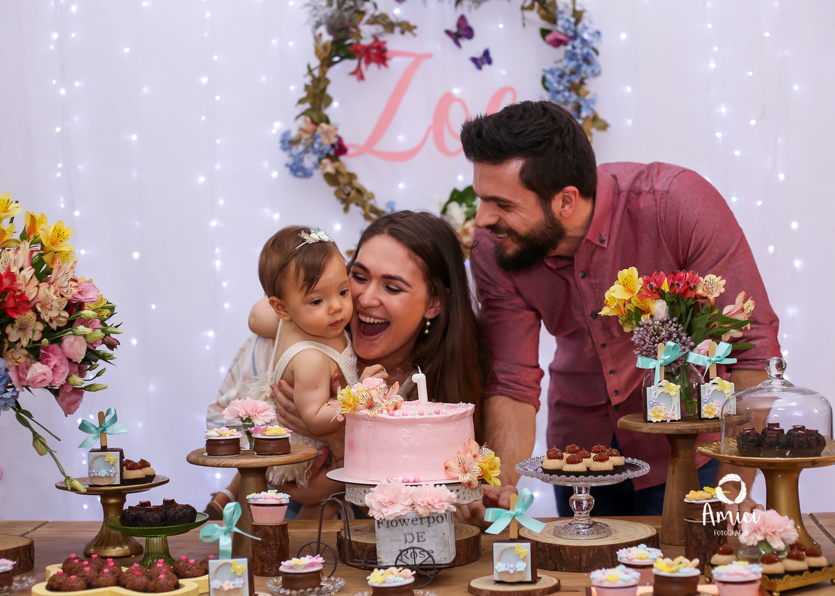 Festa infantil, bebê, mãe e pai brincando em frente ao bolo.
