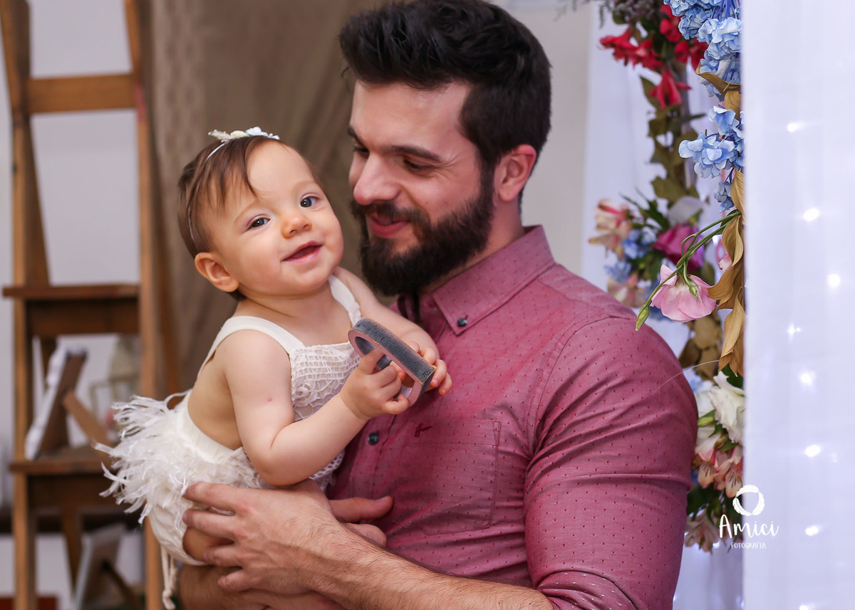 Fotografia de família, bebê brincando no colo do pai e sorrindo para a foto.