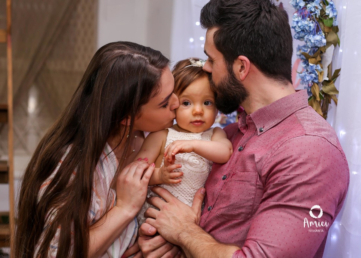 Evento infantil, beijo duplo dos pais no rosto da bebê.