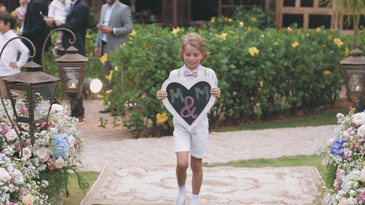 FOTOGRAFIA DE CASAMENTO PAJEN SEGURANDO PLACA COM AS INICIAIS DOS NOIVOS NA CERIMÔNIA REALIZADA NO HOTEL VILLA D'ANGELO EM ITATIBA SÃO PAULO POR HRT FILMES