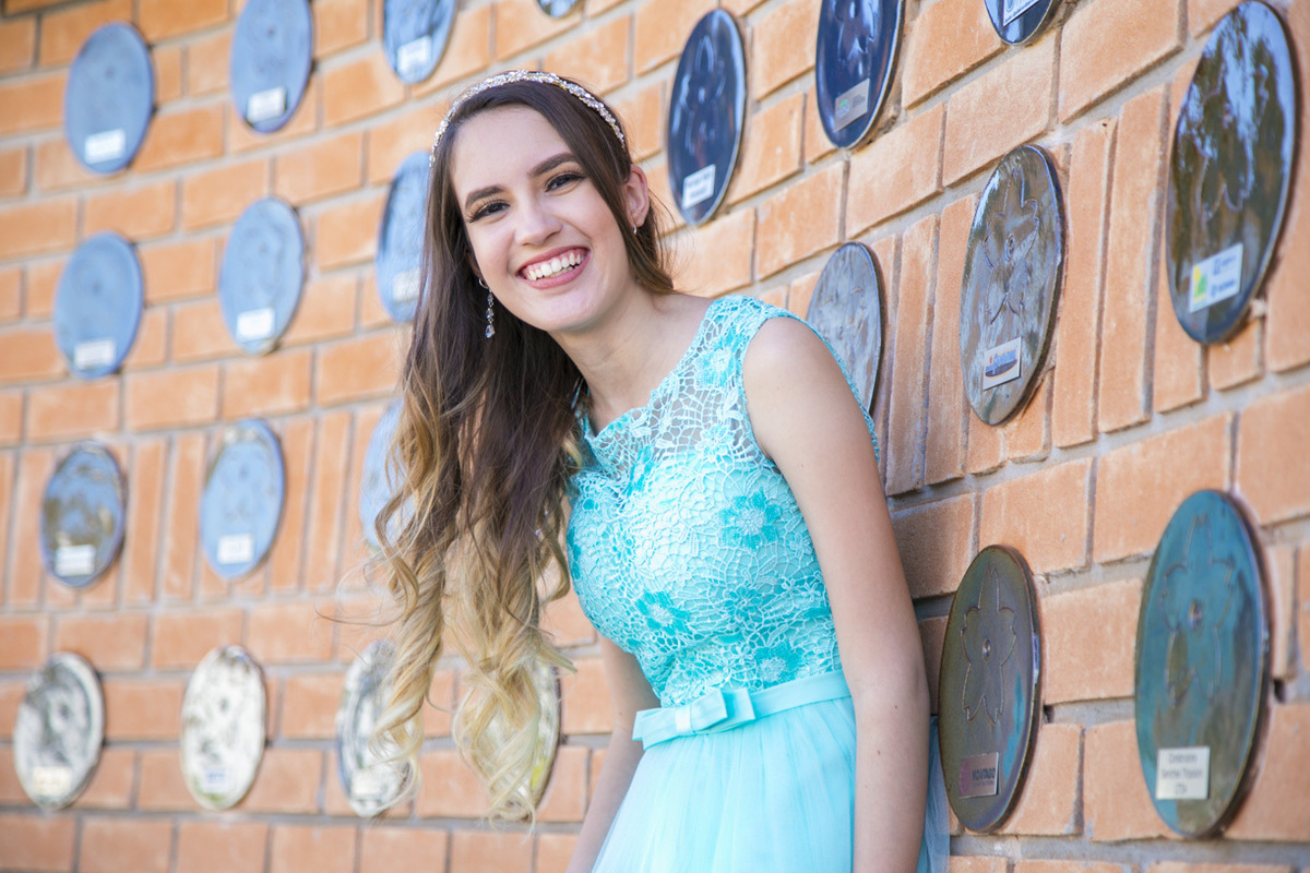 ENCOSTADA NA PAREDE E COM SORRISO NO ROSTO