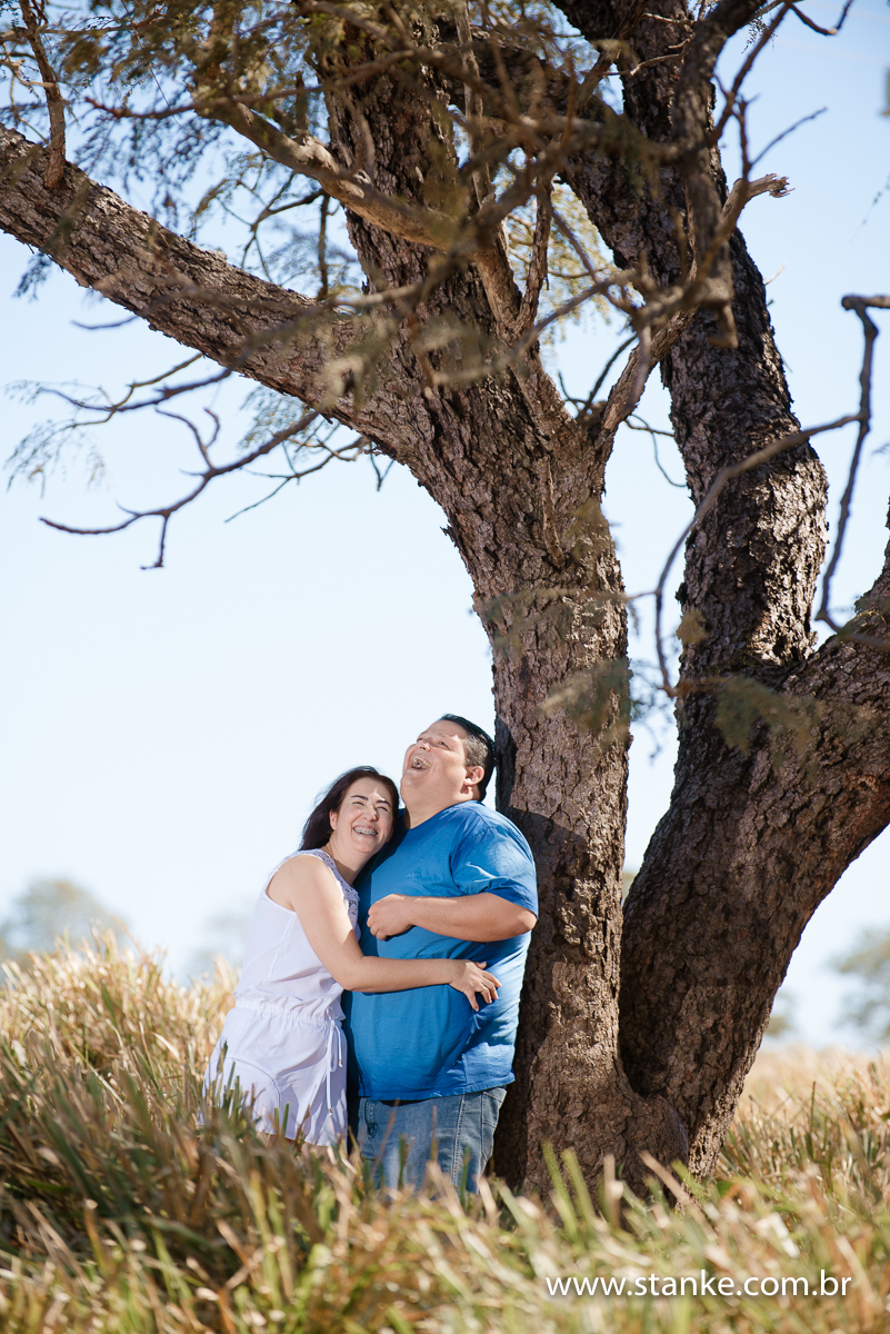 Ensaio no campo. Noivos em gargalhadas encostados na arvore na rodovia em Campo Grande Rio Negro-MS