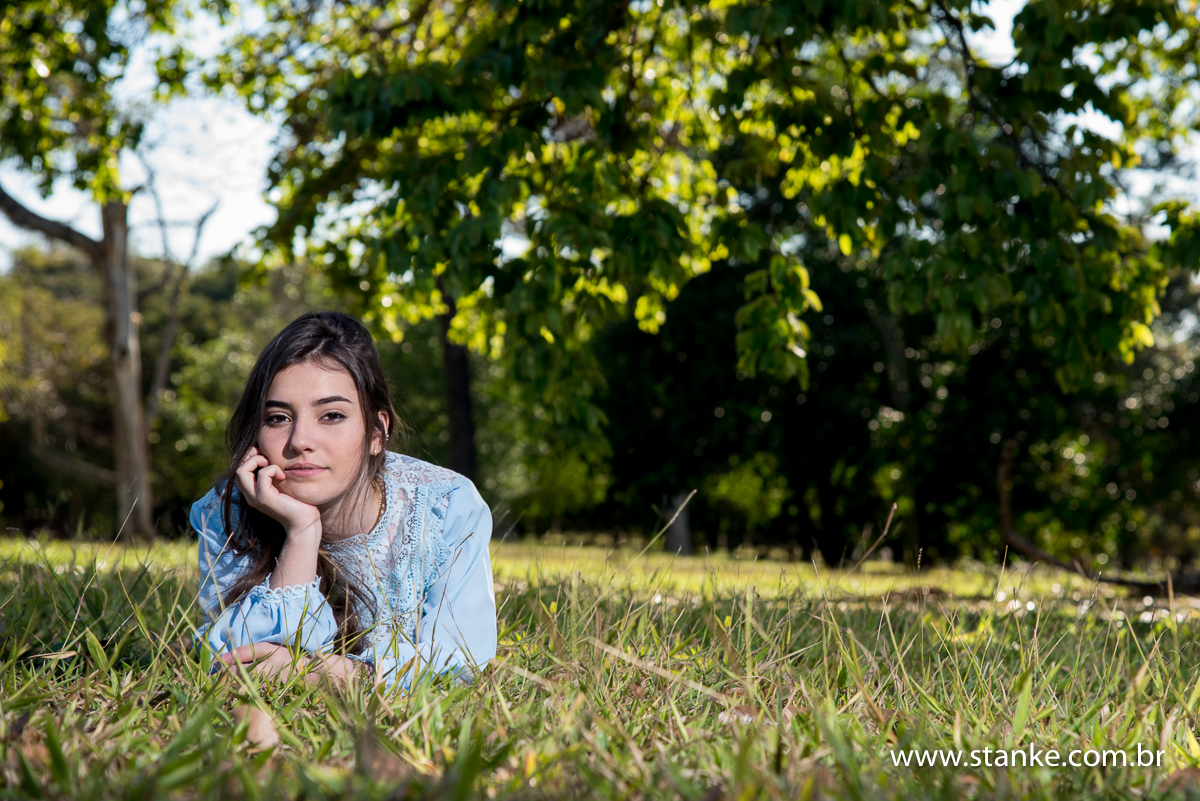 Izabelly debutante, 15 anos, deitada na grana, com a mão no rosto, no Parque das Nações Indígenas, Campo Grande-MS.