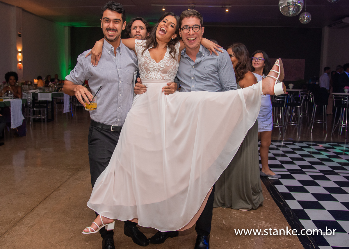 Casamento Raíra e Matheus, a noiva no colo dos amigos e o noivo olhando com aquele olhar desconfiado, no Balada Buffet, Campo Grande-MS, fotos de Pedro Stanke.