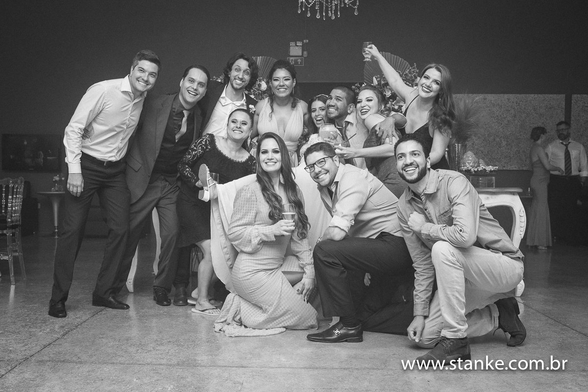 Casamento Raíra e Matheus, os noivos e amigos fazendo pose para fotos na frente da mesa do bolo, em preto em branco, no Balada Buffet, Campo Grande-MS, fotos de Pedro Stanke.
