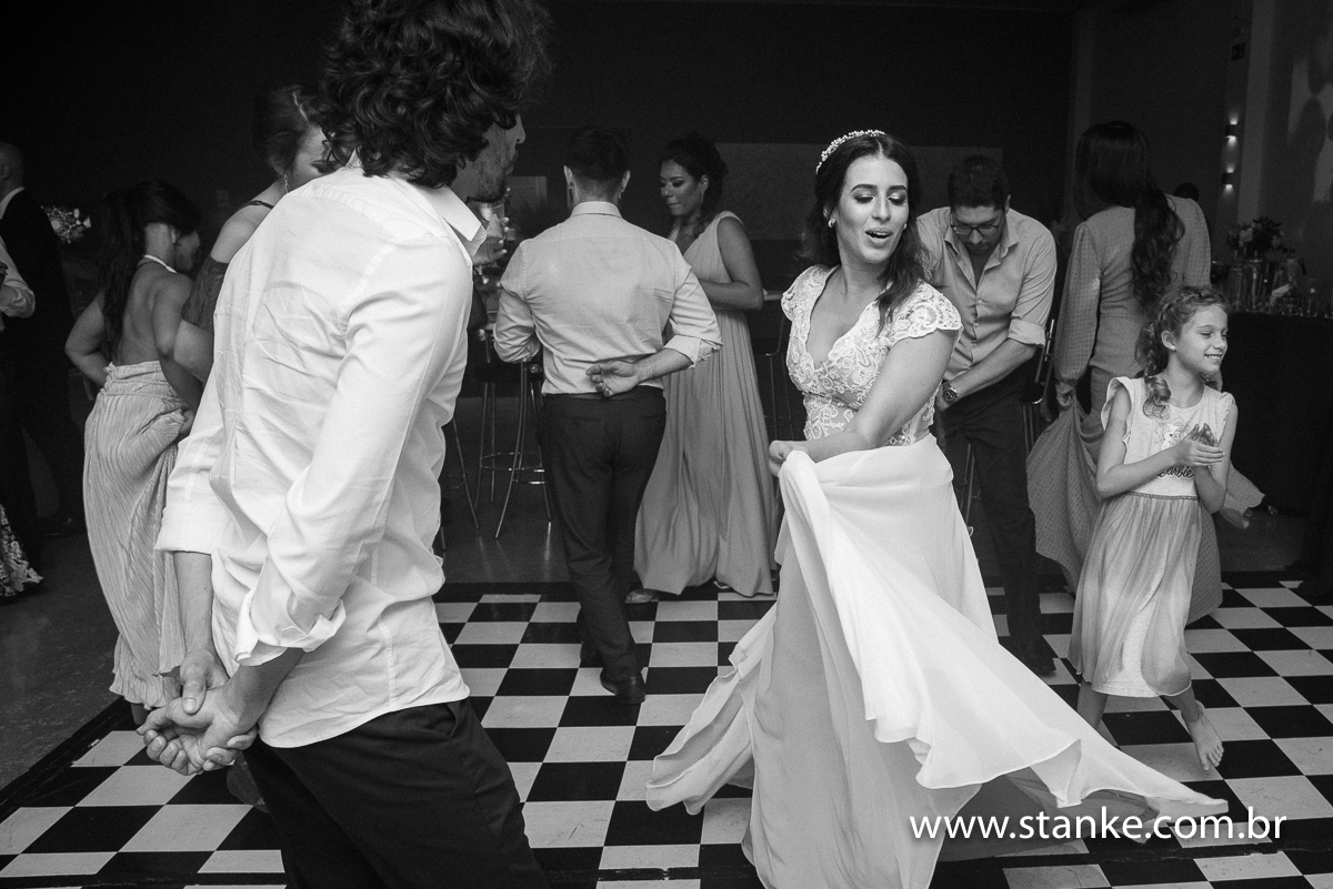 Casamento Raíra e Matheus, a noiva dançando e levantando a saia do seu vestido no meio da pista, em preto em branco, no Balada Buffet, Campo Grande-MS, fotos de Pedro Stanke.