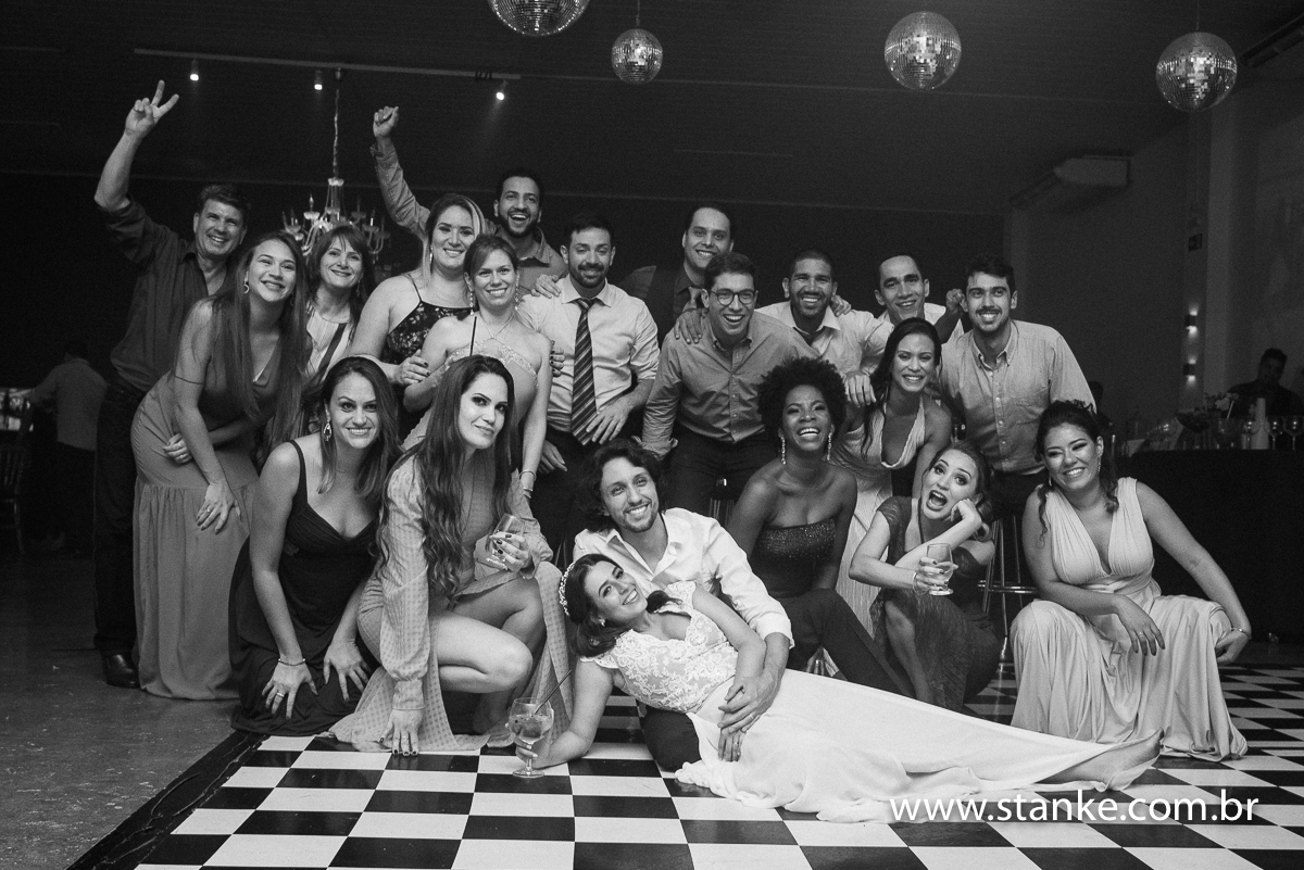 Casamento Raíra e Matheus, os noivos e seus amigos todos posando para fotos no meio da pista de dança, em preto em branco, no Balada Buffet, Campo Grande-MS, fotos de Pedro Stanke.