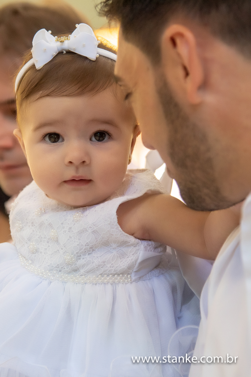 Um Close da Gabriella no colo do padrinho, com um olhar meigo, na Igreja Santíssima Trindade, em Campo Grande-MS. Fotos feitas por Pedro Stanke.