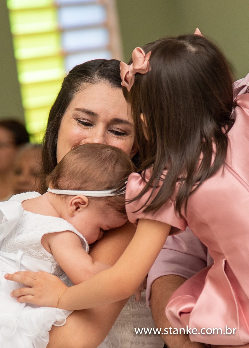 Gabriella no colo da mamãe e sua irmã mais velha no colo do pai, ambas dando um chamego na mamãe, na Igreja Santíssima Trindade, em Campo Grande-MS. Fotos feitas por Pedro Stanke.