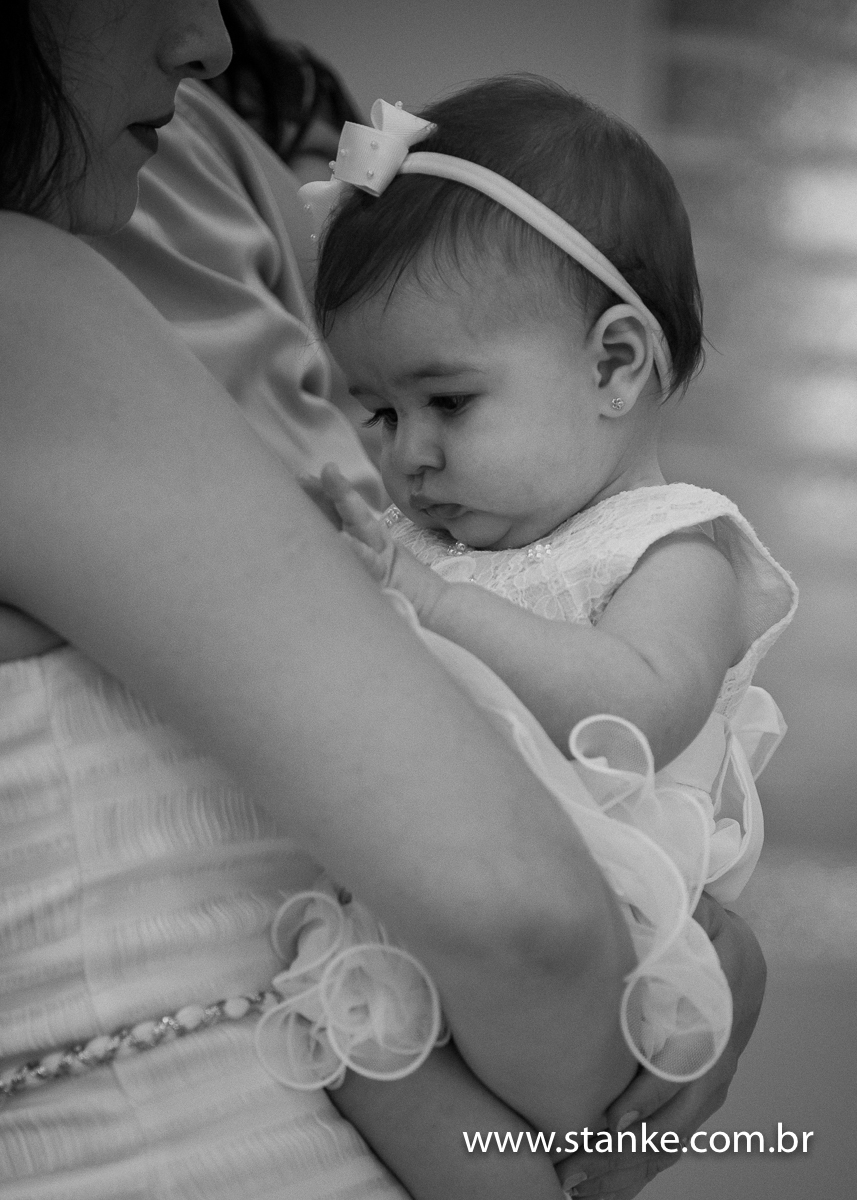 Gabriella no colo da mamãe, mexendo no vestido da mamãe super distraída, em preto e branco, na Igreja Santíssima Trindade, em Campo Grande-MS. Fotos feitas por Pedro Stanke.