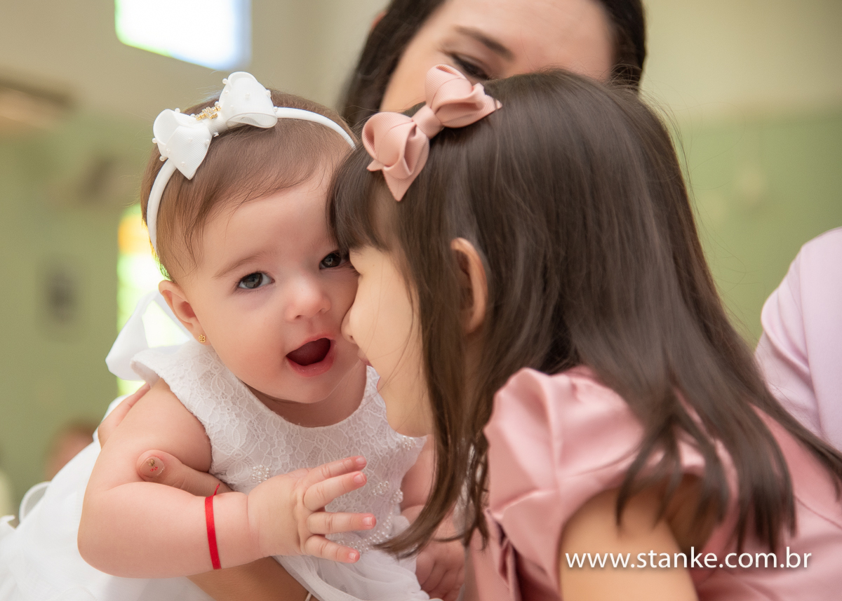 Gabriella no colo da mamãe e sua irmã mais velha no colo do pai, a mais velha fazendo carinho com o nariz na Gabi, na Igreja Santíssima Trindade, em Campo Grande-MS. Fotos feitas por Pedro Stanke.