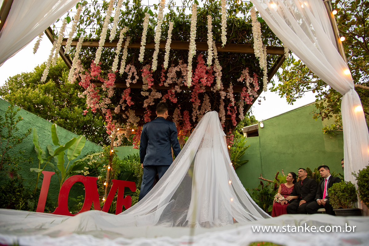 Casamento Mariana e Davi, os noivos de frente para o altar, e detalhes do degolado e noivos em baixo, com longo véu da noiva, no espaço Recanto do Sabiá. Fotos feitas feitas por Pedro Stanke.