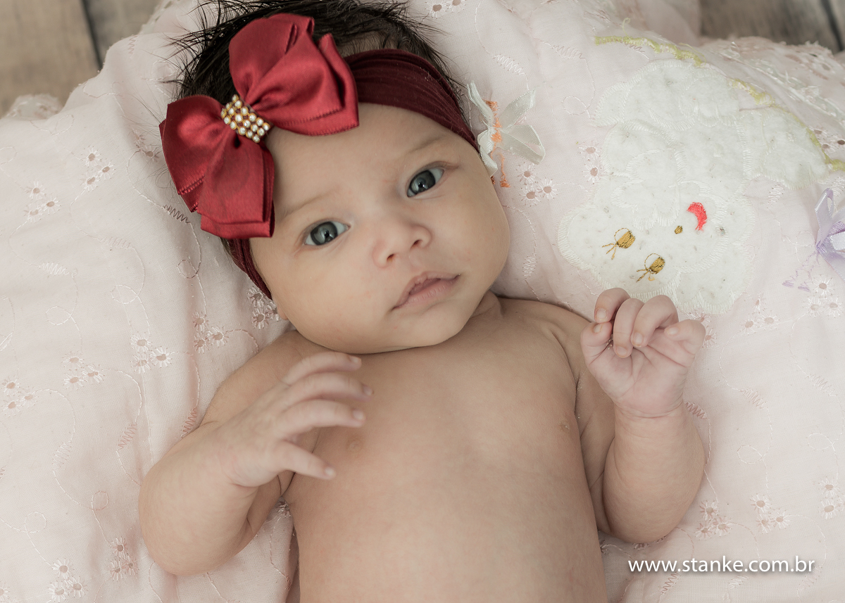 Lorena em seu newborn, com fita bordo com laço vermelho, deitadinho sobre a sua manta toda fofinha. Fotos feitas em Campo Grande-MS, pelo fotógrafo Pedro Stanke.