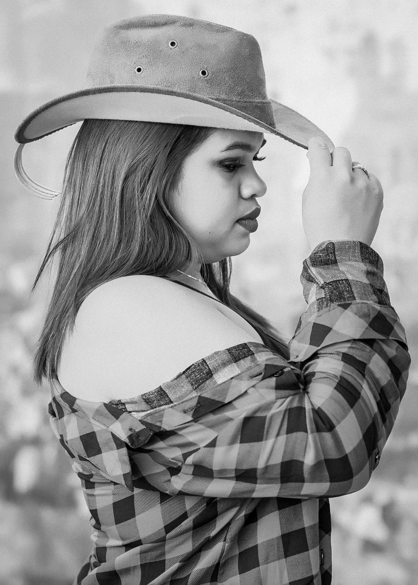 Ensaio externo Danielly, Preto e Branco, Danny de perfil segurando a aba do chapéu e com queixo baixo e sua camisa xadrez vermelha com preto caindo dos ombros. Fotos realizadas em Campo Grande-MS, feitas por Pedro Stanke.