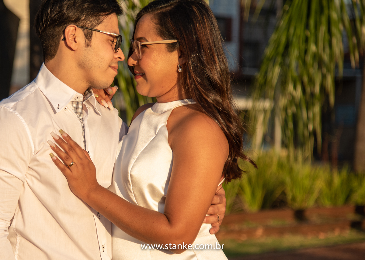 Ensaio pós casamento de Giseli e Aurélio, A Giseli com com umas das mãos no peito do Aurélio e outra no ombro e ambos se olhando com lindo sorriso. Fotos feitas no Memorial Ferroviário, em Campo Grande-MS, por Pedro Stanke.